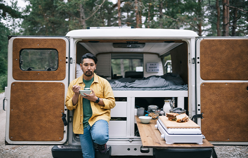 Man Eating From Bowl at Rear of Class B Motorhome with Doors Open